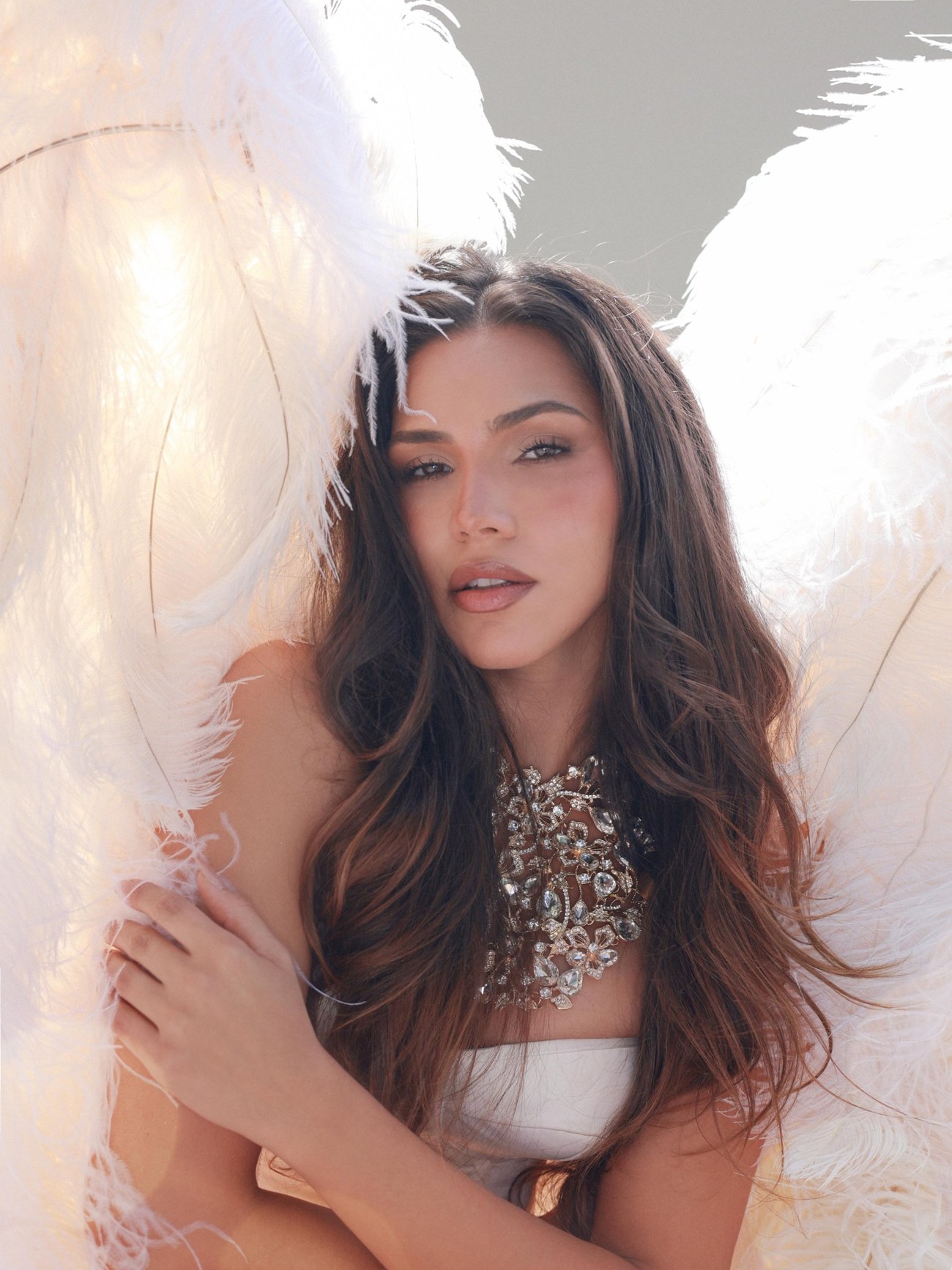 Editorial portrait with white feather wings and a crystal collar